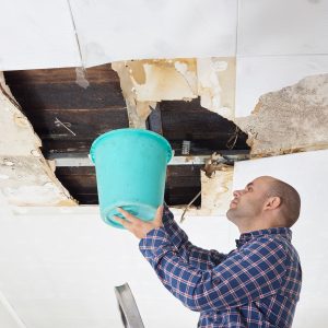 man with a bucket under leaky roof